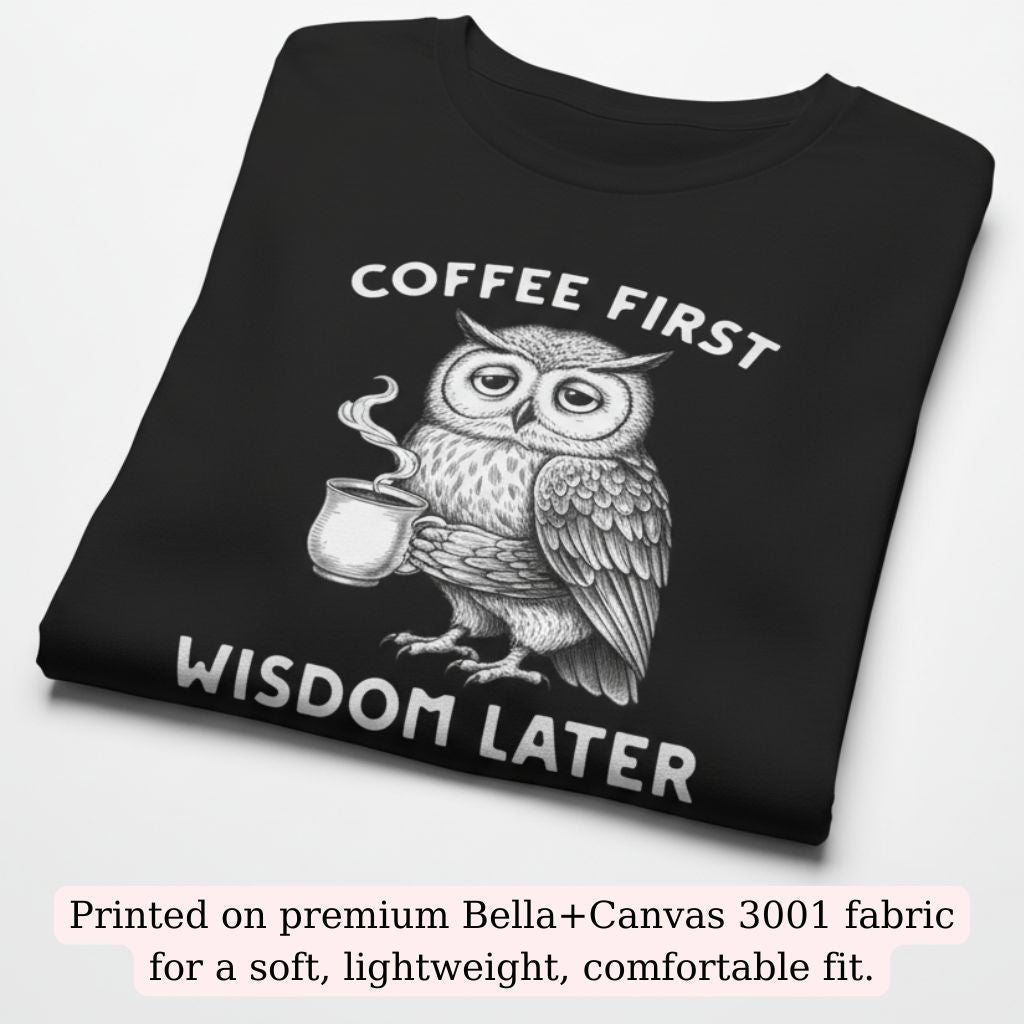 Folded black Bella+Canvas t-shirt with a cute owl illustration holding a coffee mug and the phrase “Coffee First – Wisdom Later”